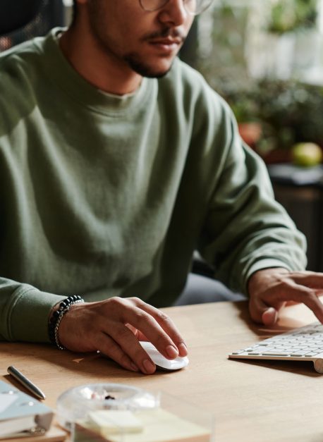 Young man in casualwear clicking mouse and pressing key Young man in casualwear clicking mouse and pressing key of computer keyboard while working over new software by workplace
